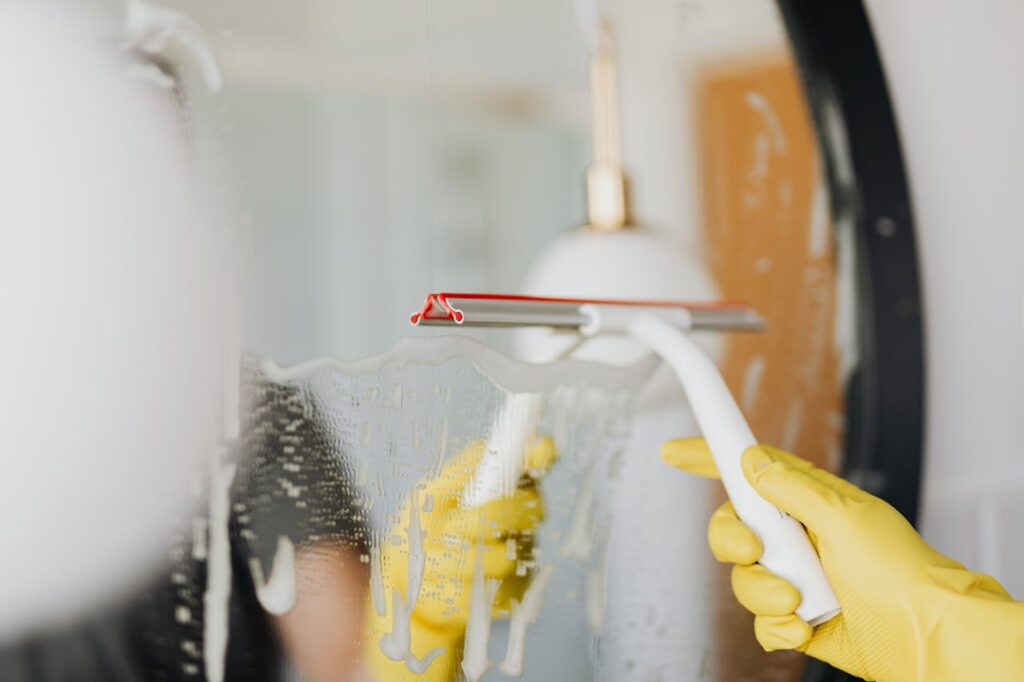 pexels photo 4239145 Person using a squeegee to clean a foamy bathroom mirror indoors.